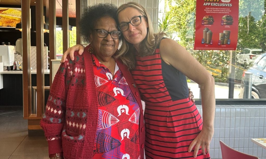 Two women in a restaurant hugging for the camera smiling 