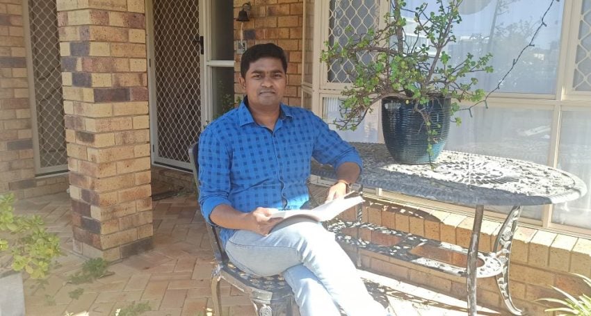 Man in blue shirt reading a book in a courtyard