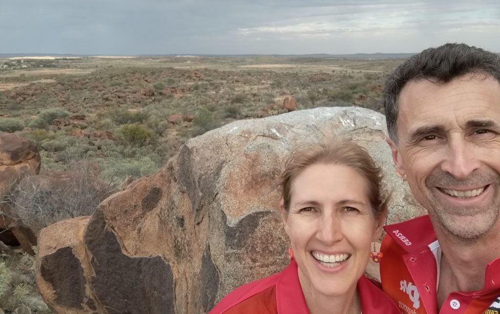 Man and woman wearing in red in the Outback smiling 