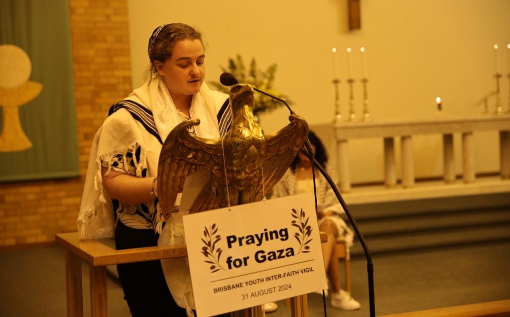 Jewish man wearing a kippah and shawl while reading from a lectern in a church 