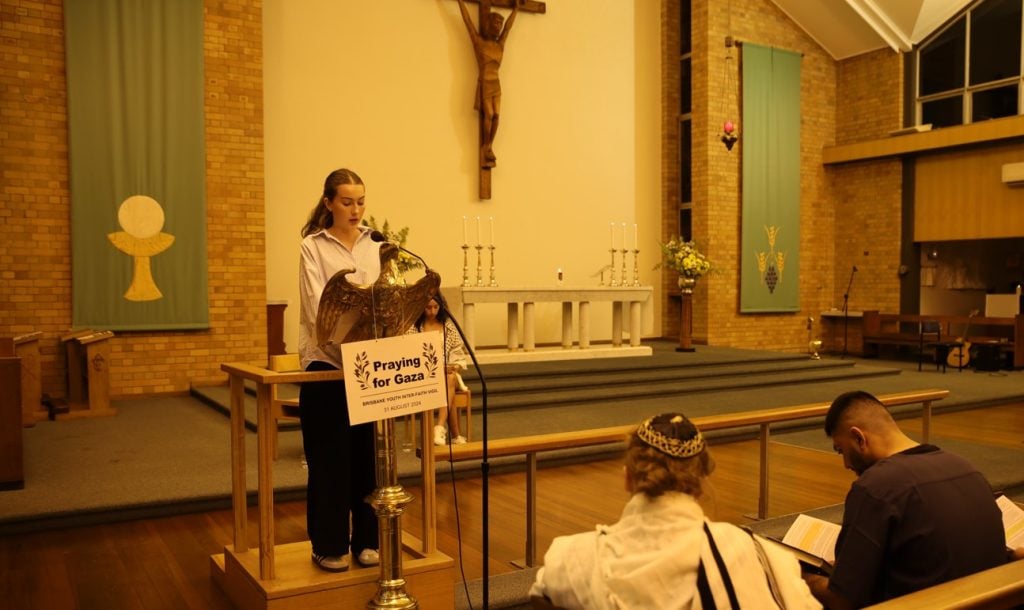 Teenage student praying in a church with a Jewish man and Muslim man in the front pew