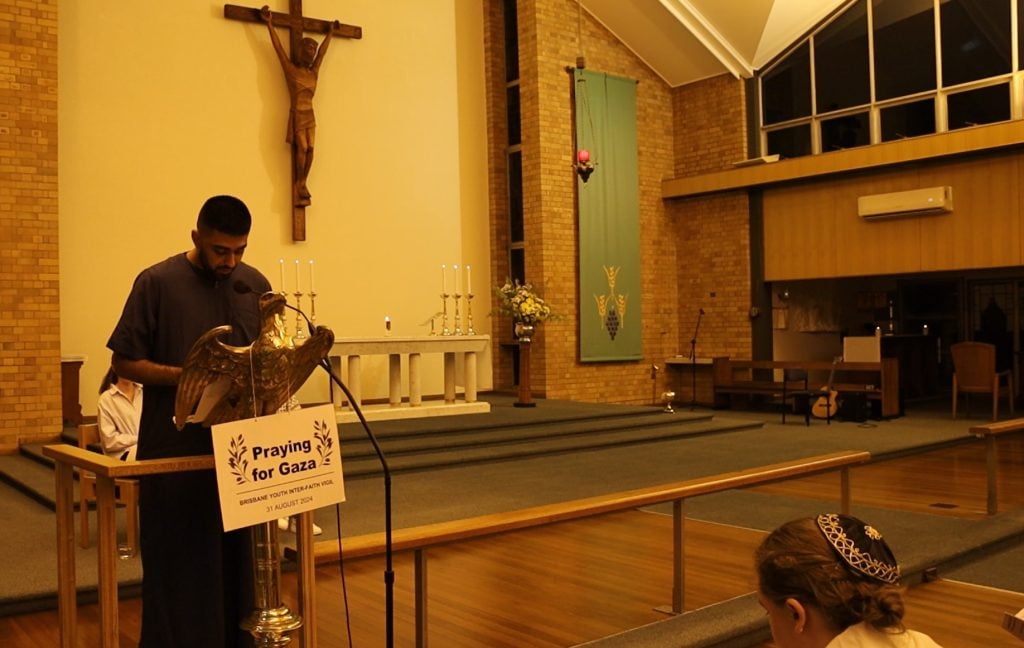 Young Muslim man wearing a thobe reading from Quran in a church