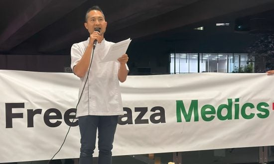 Pharmacist standing in front of a "Free Gaza Medics" sign giving a speech