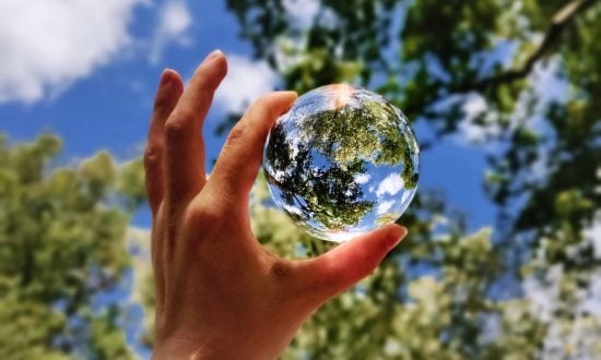 A hand holding a clear globe to the sky with trees and clouds in the background