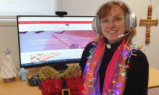 Woman priest wearing tinsel and lights in front of a computer