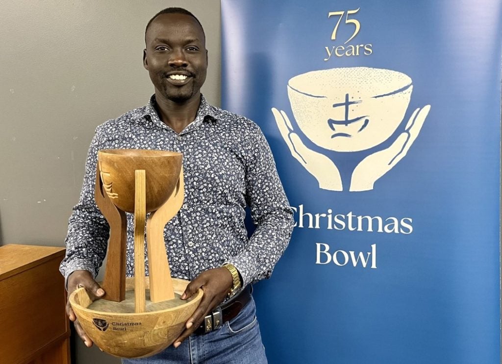 Smiling CEO man in shirt and jeans holding a wooden bowl in front of a blue banner sign 