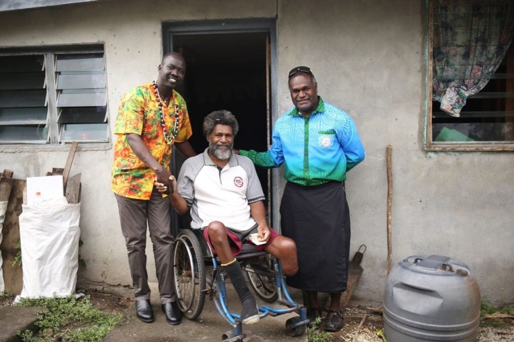 Two men standing and one in a wheelchair in the Pacific 