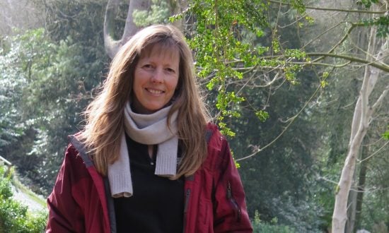 Woman wearing scarf and red jacket in New Zealand bush, looking at the camera smiling