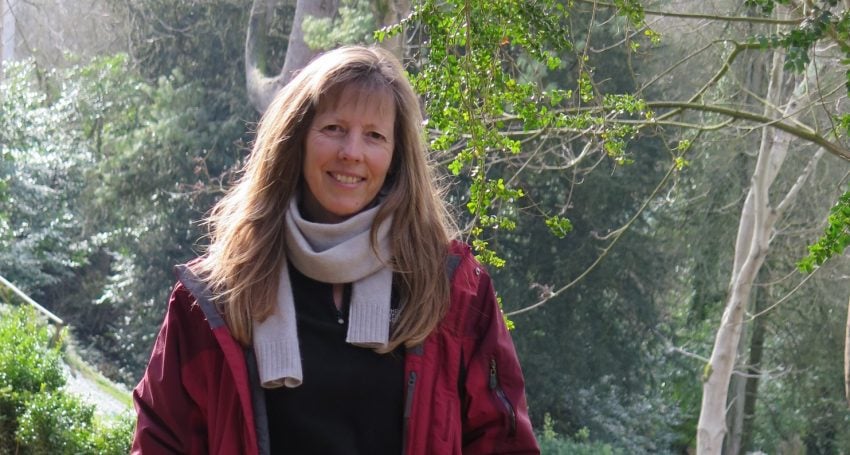 Woman wearing scarf and red jacket in New Zealand bush, looking at the camera smiling