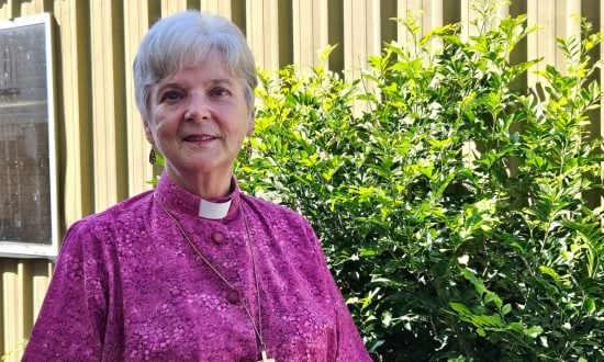 Woman bishop in purple shirt and collar standing outside