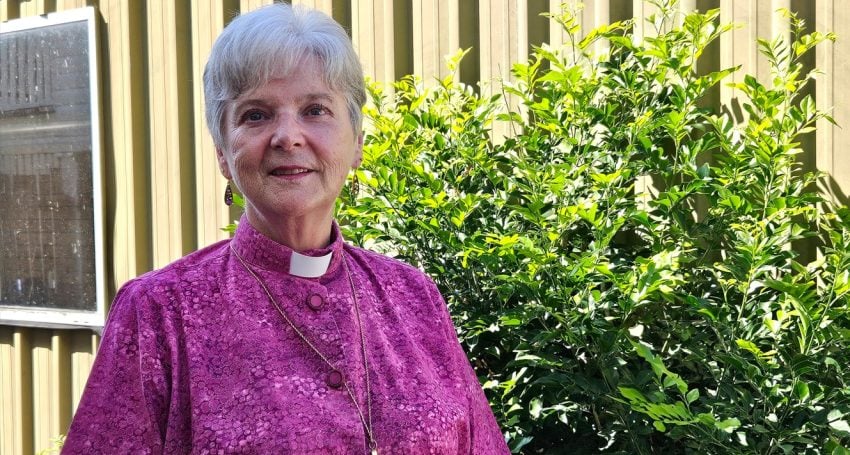 Woman bishop in purple shirt and collar standing outside