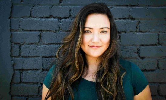 Young woman in teal t-shirt standing against dark brick wall