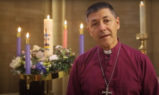 Archbishop wearing a purple shirt and pectoral cross standing in front of lit advent candles in a Cathedral