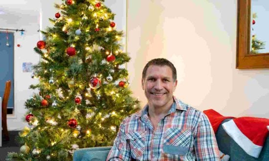 Man in plaid shirt sitting next to a Christmas tree