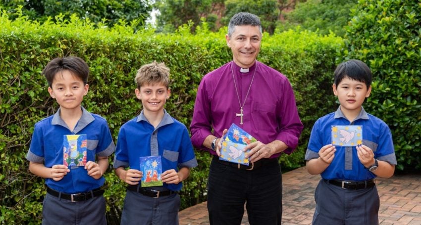 Archbishop with three school boys holding up Christmas card designs