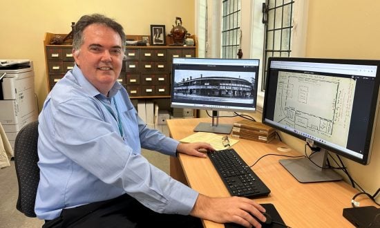 Man in blue shirt at a computer with artefacts behind him