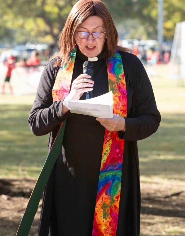 Priest n black robes and colourful stole holding a microphone 