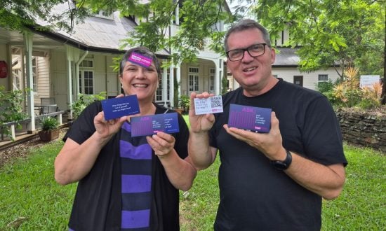 Man and woman holding purple cards while standing outside and smiling at the camera