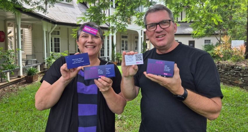 Man and woman holding purple cards while standing outside and smiling at the camera