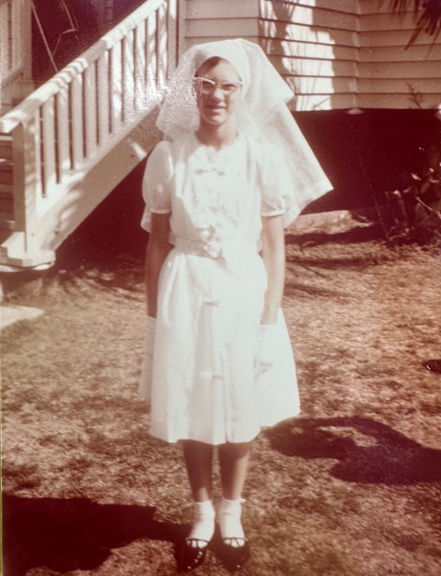 Girl in white confirmation garb outside her home in the 1960s