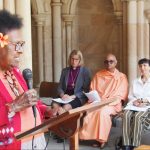 Torres Strait Islander elder with a flower in her hair speaking outside a limestone cathedral