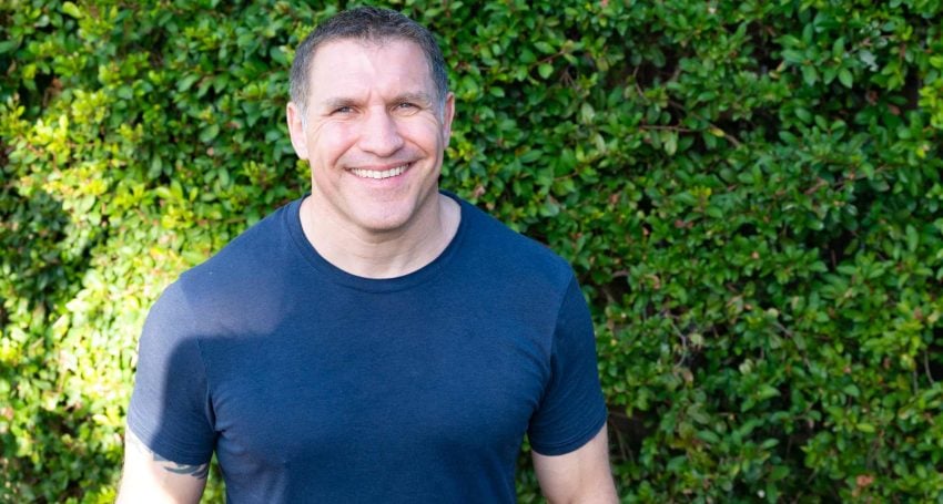 Man in dark blue t-shirt in front of a green bush