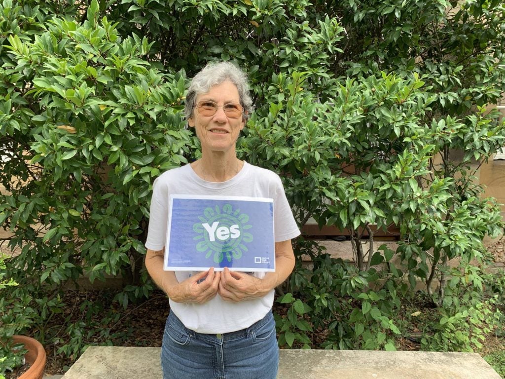 Woman in white shirt and blue jeans holding a Yes23 sign