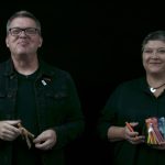 Man and woman wearing black in front of black screen smiling