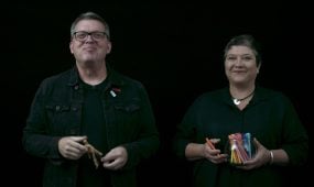 Man and woman wearing black in front of black screen smiling