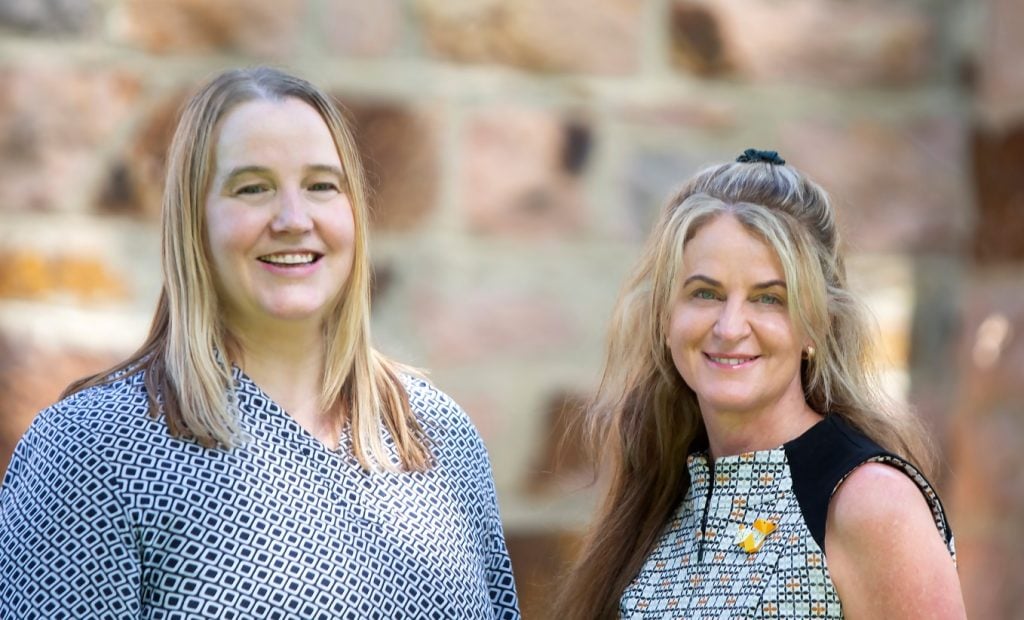 Two women standing in front of limestone bricks smiling at the camera