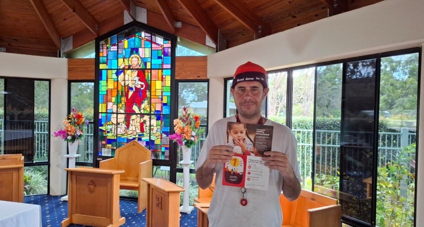 Alexi Malmgren standing in church holding up a promotional flyer