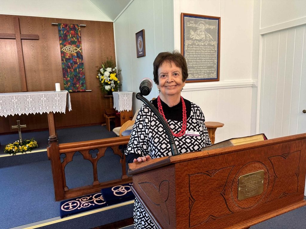 A woman stands in a church hall posing for a photograph