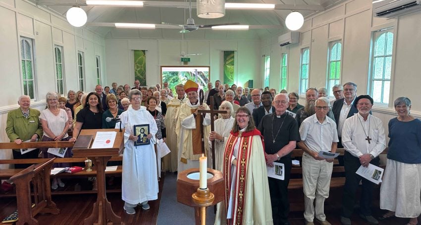 A large group of people stand in a church hall posing for a photograph