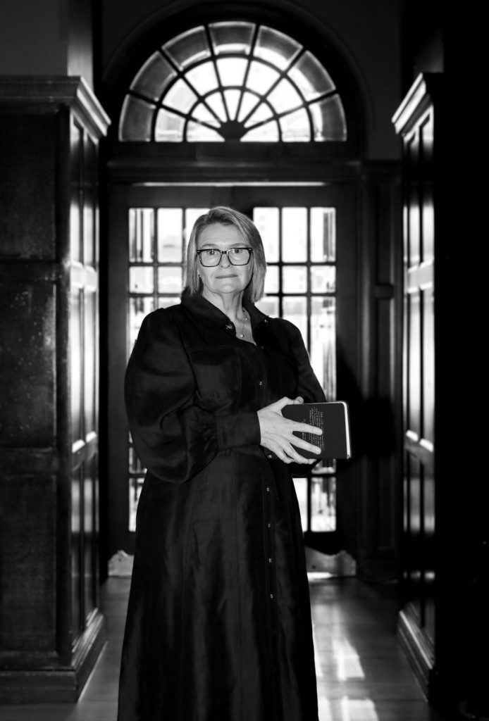 A woman stands in a hallway holding a book