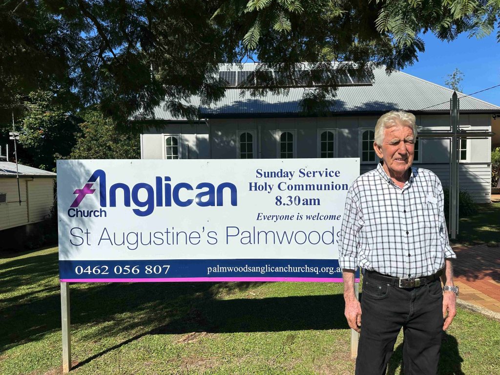 A man stands in front of church signage for St Augustine's Palmwoods church