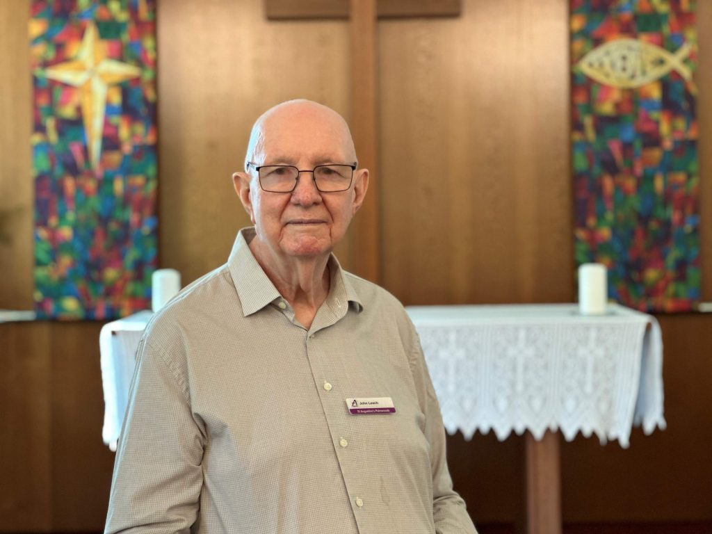 A man poses for a photograph in front of a large crucifix on the wall of a church