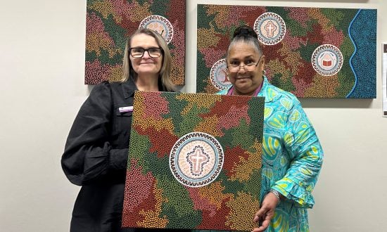 Two women pose for a photo holding up a First Nations artwork