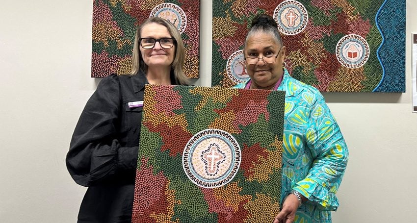 Two women pose for a photo holding up a First Nations artwork