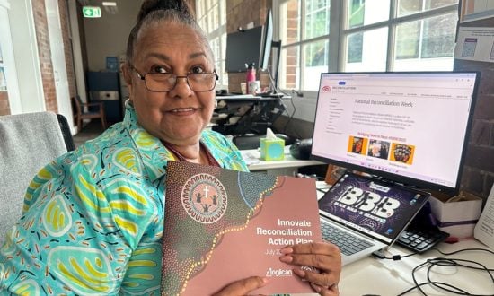 Aboriginal elder holding up a RAP document in front of a PC in her office
