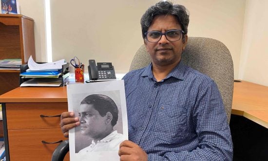The Rev’d Stephan Prabu seated in an office holding a picture of Vinayak S Masoji