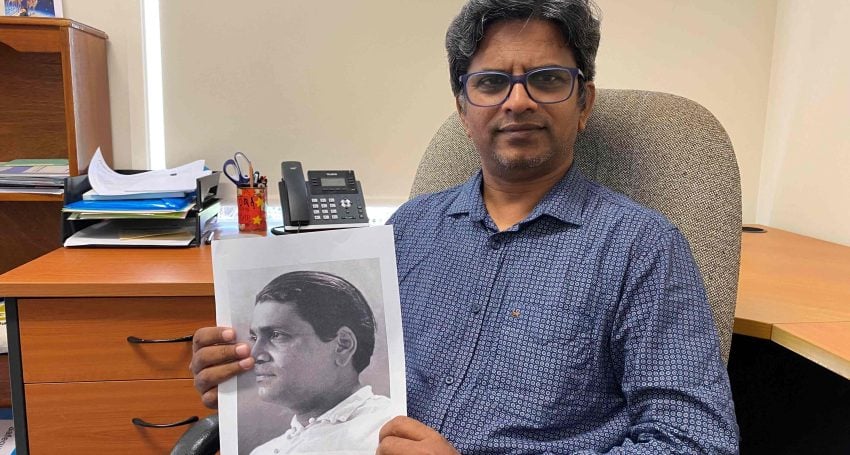 The Rev’d Stephan Prabu seated in an office holding a picture of Vinayak S Masoji