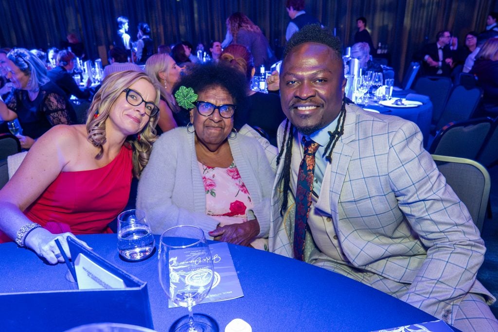Two women and a man pose for a photograph at a gala event