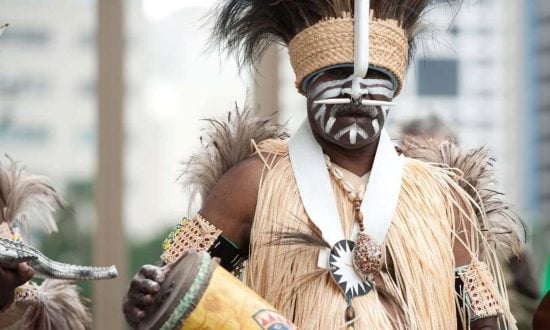 A man wearing a headdress and traditional clothing holds a musical instrument