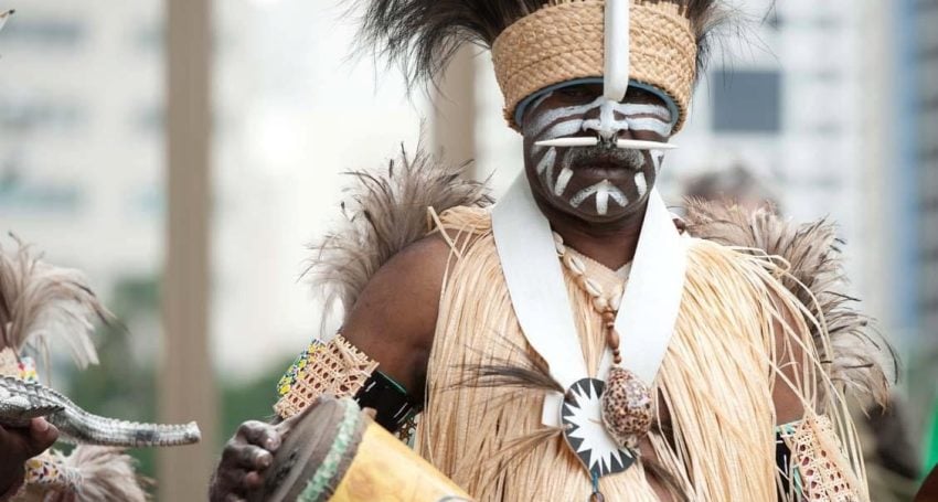 A man wearing a headdress and traditional clothing holds a musical instrument