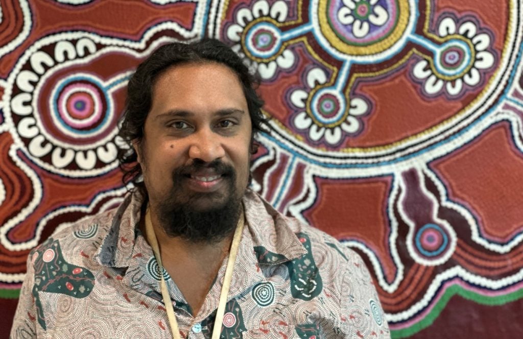 Aboriginal man standing in front of Aboriginal artwork
