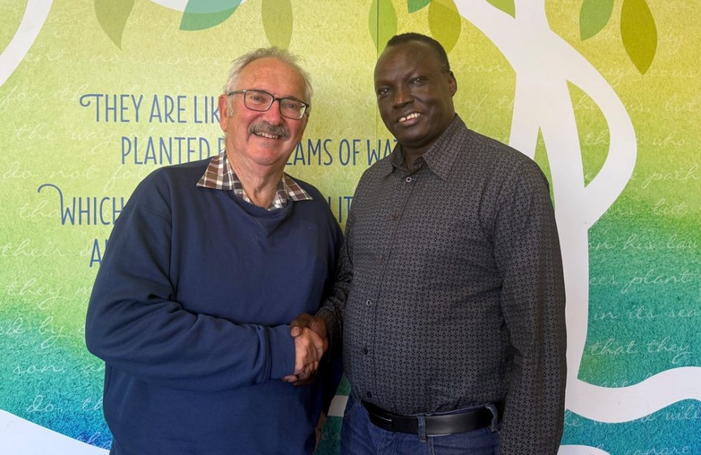 Two men shaking hands in front of a colourful wall in a church