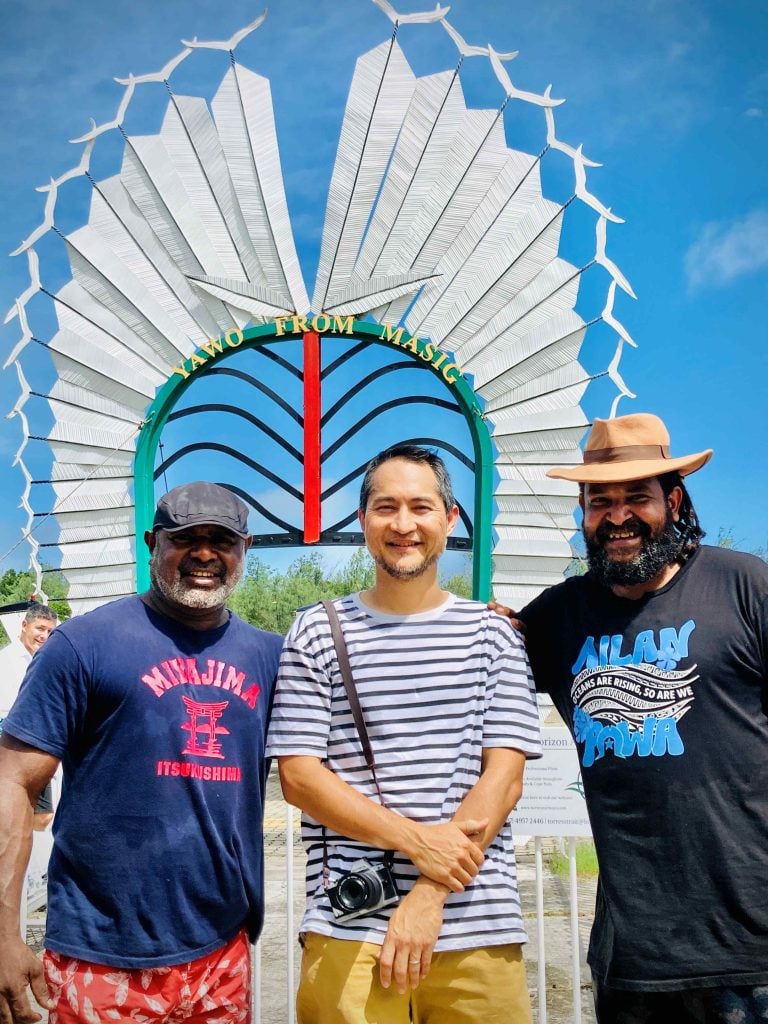 Three men pose for a photograph while standing outside a sculpture