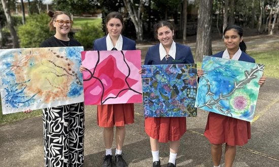 A teacher and three students hold up paintings
