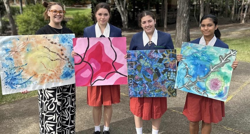 A teacher and three students hold up paintings