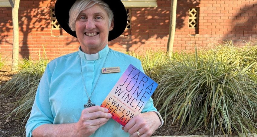Woman priest in blue shirt wearing an Akubra hat and holding a book